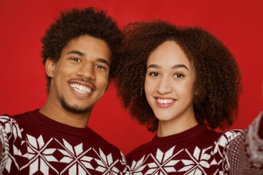 Akıllı telefondan çekilmiş bir çift fotoğrafı ve karantina covid-19 'da yeni yılı ve Noel' i kutlarken çekilmiş. Kazaklı mutlu erkek ve kadın kırmızı arka planda izole edilmiş kameraya bakıyor.