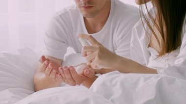 Genç bir çift yatak odasında dinleniyor, ellerine dezenfektan sürüyor. Güneş ışığı perdelerin arasından süzülerek huzurlu evlerinde sıcak ve samimi bir atmosfer yaratır..