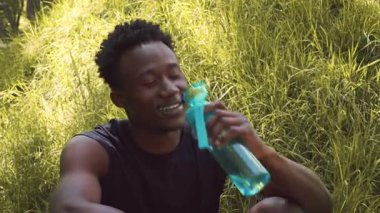 Genç bir Afrikalı Amerikalı adam, halka açık bir parkta egzersiz yapıyor, gülümseyerek, doğa ile çevrili sağlıklı yaşam tarzının tadını çıkarıyor. Atmosfer canlı ve canlandırıcı..