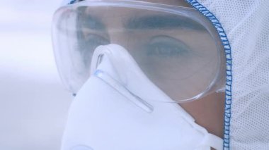 Koruyucu giysiler giymiş genç bir Orta Doğulu kadın dışarıda dikiliyor, odaklanmış ve özenli. Kalabalık bir şehir ortamında sağlık ve güvenliğe karşı ihtiyatlı bir yaklaşım sergiliyor..