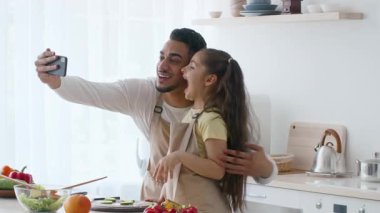 Bir baba ve kızı aydınlık bir mutfakta neşeli bir anı paylaşıyorlar. Bir yemek hazırlıyorlar, gülümsüyorlar ve etrafları yeni malzemelerle çevriliyken bir akıllı telefonla anı yakalıyorlar..