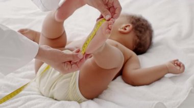 Bebeklerin ayaklarını ölçen bir bakıcı, yumuşak bir yüzeyde yatan bir bebek. Çocuk rahat bir şekilde giyiniyor ve nazik bir şekilde ilgi görüyor. Kapalı alandaki yakınlaşma anını vurguluyor..