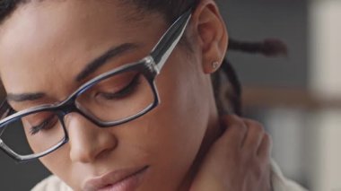 Genç bir Afrikalı Amerikalı kadın çevrimiçi öğretmenlik yaparken boyun ağrısı çekiyor. Ev idaresi gibi giyinmiş, uzaktan eğitimin zorluklarını gösteriyor..