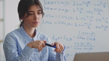 Genç bir kadın evinden çevrimiçi bir ders veriyor, öğrencileri dinamik içerikli ve net açıklamalarla meşgul ederken bilgisayarını kullanıyor ve karmaşık konuları ele alıyor..