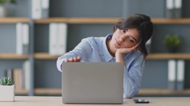 Uzaktan eğitim seansına katılan genç bir kadın laptopuyla etkileşime girerken düşünceli görünüyor. Modern çalışma alanı parlak ve organize, çevrimiçi öğrenmeyi vurguluyor.