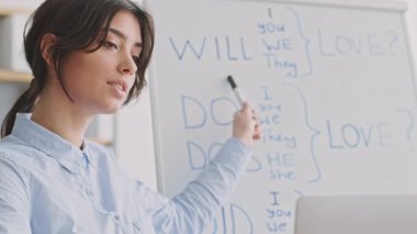 Genç bir kadın evinden ilgi çekici bir online ders veriyor. Bir dizüstü bilgisayarla etkileşime geçiyor, öğrencilere kişisel eğitim sağlıyor ve bir yandan da öğretmek için beyaz tahta kullanıyor..