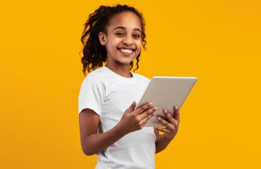 E-öğrenme. Dijital tablet kullanan mutlu Afrika kökenli Amerikalı kız. İnternette ödev yapıyor. Sarı Stüdyo 'nun arka planında tek başına duran kameraya bakıyor. Boş Alanı Olan Pankart