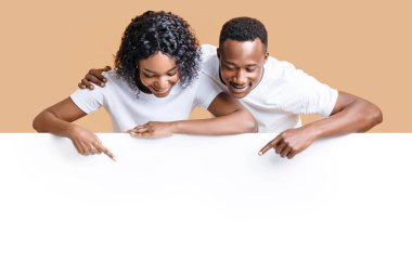 Meraklı Afrikalı Amerikalı çift sarı stüdyo arka planındaki boş reklam panosuna işaret ediyor. Neşeli genç siyah erkek ve kadın reklam ya da metin için boş alan gösteriyor.