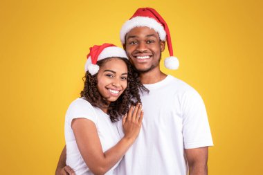 Noel Baba Şapkalı Afrikalı çift stüdyoda sarılıp, kameraya gülümsüyor. Xmas ve Yeni Yıl Neşe, Kış Tatili Kutlama Konsepti.