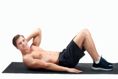 Gülümseyen milenyum çocuğu çıplak göğsüyle spor paspası üzerinde egzersiz yapıyor arka planda, panoramada. Vücut kaslarını çalıştıran, formda olan sporcu portresi.