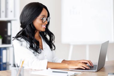 İş yerinde dizüstü bilgisayar kullanan ve klavyede yazan mutlu bir ofis çalışanı. Genç siyah yönetici e-postayı kontrol ediyor, iş bilgilerini internette arıyor, online görüşme yapıyor