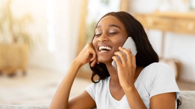 Afro-Amerikan bir kadının portresi cep telefonuyla kapalı alanda arama yapıyor. Gülümseyen siyahi iş kadını ev telefonundan iş arkadaşıyla konuşuyor.