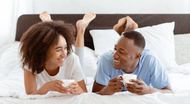 Sabah ya da hafta sonu boş zaman, yatakta kahvaltı ve evde yalnızlık. Neşeli Afro-Amerikan erkek ve kadın milenyumu yalan söylüyor, konuşuyor, sıcak çay içiyor, yatak odasında bir tepsi kruvasanla.