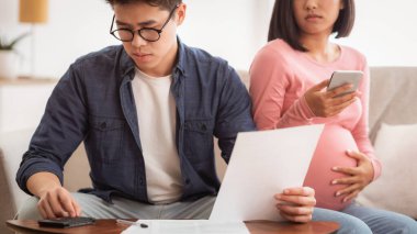 Faturalara bakan endişeli Asyalı çift evdeki koltukta oturan mali krizle boğuşan faturalara bakıyor. Borç ve İflas, Aile Mali Sorunları Konsepti. Seçici Odaklanma