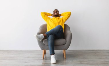 Tembel hafta sonu. Afrikalı Amerikalı Adam, gözleri kapalı, elleri başının arkasında oturan gri kapüşonlu, sarı kapüşonlu. Rahatlama ve Rahatlık Konsepti