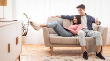 Mutlu Koreli Çiftler Evde Oturma Odasında Otururken Dizüstü bilgisayar izleyip, interneti birlikte gezip, rahatlıyor. Modern Yaşam, Haftasonu Yaşam Tarzı. Boşluğu Kopyala