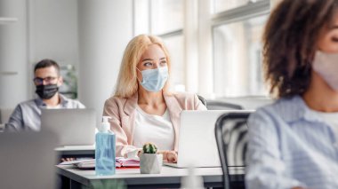 Karantina sonrası şirket çalışanlarının işi. Masalarında dizüstü bilgisayarları ve antiseptikleri olan koruyucu maskeli çok ırklı işçiler, yöneticiye odaklanmış, ofisin içindeki pencereden dışarı bakıyor.