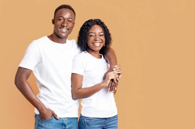 Sarı arka planda kucaklaşan ve gülümseyen neşeli siyah çift. Mutlu Afrikalı genç Amerikalı adam gülümseyen kız arkadaşına sarılıyor, birlikte poz veriyor, mekanı kopyalıyor. Aşk, ilişkiler konsepti