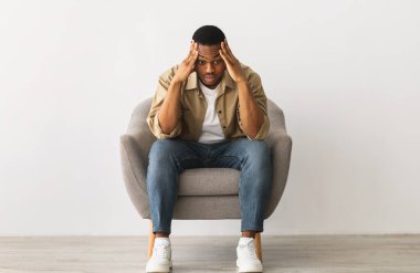Endişeli Afrikalı Amerikalı Adam, kafaya dokunmanın sorun yaratacağını düşünüyor ve endişeleniyor. İçerideki gri duvarın arkasında oturuyor. Depresyon ve Erkek Akıl Sağlığı, Stresli Hayat