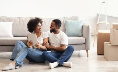 Yeni Ev 'e taşınıyorum. Siyah Çifti Sevmek Dijital Tablet Kullanarak Yerlerde Oturarak Açık Kutular Arasında İnternet Tarayarak. Yeni Apartman 'a taşınma. Gayrimenkul Sahipliği Konsepti. Boş Alan