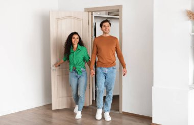Smiling couple opening door and walking in their apartment, entering new home, happy cheerful young guy and lady standing in doorway of modern flat, looking at design interior together, coming inside