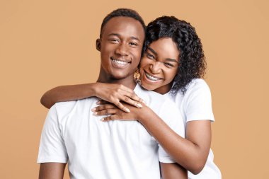 Sarı stüdyo arka planında sarılan mutlu Afro-Amerikan genç erkek ve kadın portresi. Neşeli siyahi aşıklar sarılıyor, duygusal bir bayan neşeli erkek arkadaşına arkadan sarılıyor, yakın plan.