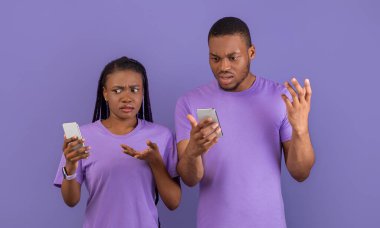 Garip Mesaj, Kötü Haber, İnternet Bağlantısı Sorunu. Kafası karışmış binlerce yıllık Afrika kökenli Amerikalı çift telefonlarına bakıyor ve omuzlarını silkiyor, mor menekşe arka planda tek başlarına duruyorlar.