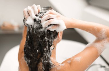 Kadın şampuan sürüp, banyo yaparken modern banyoda banyo yaparken geri dönüş görüntüsü. Saç bakım rutini yapan kadın kozmetik kullanıyor. Güzellik ve Saç Bakımı Konsepti. Seçici Odaklanma