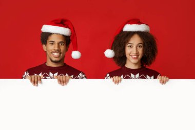 Kış havası ve Noel kutlaması. Neşeli Afro-Amerikan arkadaşları ya da Xmas kazak ve şapkalı aileleri, beyaz posterli, kırmızı arka planda izole edilmiş, stüdyo çekimleri