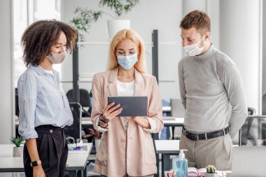 Yeni görev, sosyal uzaklık ve tecritten sonra ofis işi. Koruyucu maskeli genç iş kadını Avrupa 'lı adama ve ofisteki Afro-Amerikan bayana görev veriyor.