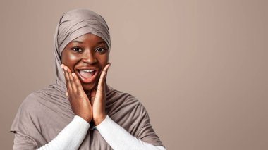 Heyecan içindeki tesettürlü siyahi kadın, Afrikalı neşeli Müslüman bayan iyi habere duygusal tepki veriyor, Işık Stüdyoları 'nın arkasında duruyor, kameraya bakıyor, boşluğu kopyalıyor.