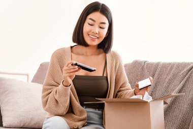 Ürün İncelemesi. Neşeli Asyalı kadın portresi makyaj malzemeleriyle hediye güzellik kutusunu aldı, makyaj için göz falı paleti tuttu, karton paketleri açtı, evdeki kanepede oturdu.