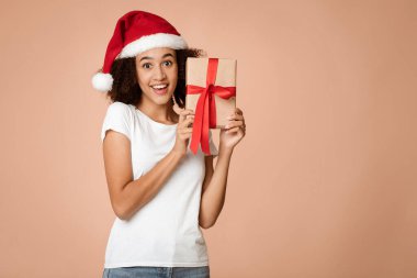 Kış tatilleri ve hediye fikirleri. Şaşırmış genç Afro-Amerikan kadın Xmas şapkalı genç adam hediyesiyle şaşırmış, kameraya ağzı açık bakıyor, arka planda izole edilmiş, boş alan, stüdyo çekimi.