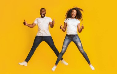 Mutlu Siyah Adam ve Kadın Havada Atlama ve Thumbs Up, sarı arka plan gösteren