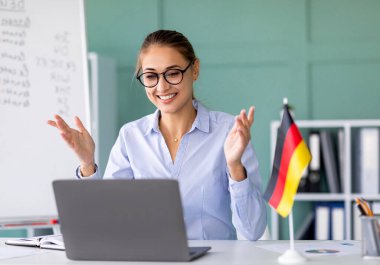 Öğretmenle e-öğrenme, sosyal uzaklık, yeni normal. Diz üstü bilgisayar kullanarak Almanca dersi veren mutlu bayan öğretmen. Genç öğretim üyesi internette öğrencilere dil bilgisi kurallarını anlatıyor