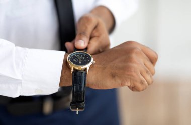 Tanımlanamayan Afro-Amerikan iş adamının pahalı kol saati takıp deri bantlı şık takım elbiseli şık bir erkek ve sabahları işe hazırlanan beyaz gömlekli fotoğrafı.