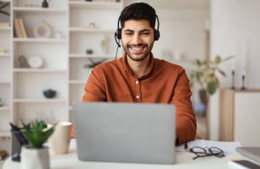 Modern İçişleri Bakanlığı 'nda bilgisayarla çalışan gülümseyen Orta Doğulu Erkek Yöneticinin portresi, masada oturan ve müşterilere danışmanlık yapan mutlu adam PC kullanıyor, ücretsiz kopyalama alanı kullanıyor.