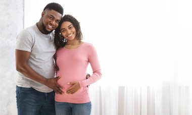 Genç, evde poz veren Afrikalı bir çift bekliyor. Pencerenin yanında duruyorlar ve gülümsüyorlar.