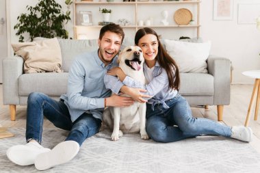 Mutlu Aile Kavramı. Modern apartmanda yerde oturan köpekli güzel bir çiftin portresi.