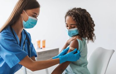 Çocuklar için vax. Tıbbi İşçi Siyah Ergenlik Öncesi Aşı Yapıyor, Aşı Yapıyor ve Koluna Yapıştırıcı Bandaj Yapıyor Yüzü Maske Takıyor Klinikte. Coronavirus Koruma Konsepti