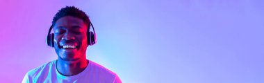 Kulaklık takan yakışıklı genç bir adam, kapalı gözlerle müzik dinliyor, afiş tasarımı yapıyor. Mutlu Afrikalı Amerikalı adam yeni şarkı listesinin keyfini çıkarıyor ve gülümsüyor