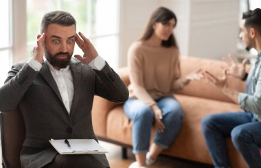 Evlilik terapisi. Genç bir çiftin, ofisinde duygusal tartışmalar, kavga etmeleri ve birbirlerine bağırmaları, koltukta oturmaları, seçici bir şekilde odaklanmaları karşısında aile danışmanının kafasını kavraması şok edici.