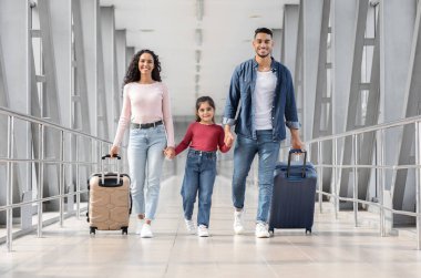 Tatile hazırım. Havalimanı Terminali 'nde çantalarla yürüyen mutlu bir Orta Doğulu aile küçük kızı olan gülümseyen bir Arap ebeveyn el ele tutuşuyor, birlikte seyahat etmekten keyif alıyor,