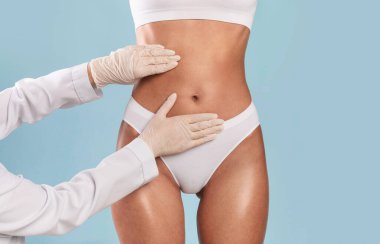 Mükemmel Vücut yapmak. Plastik cerrahi kliniğinde muayene olan tanınmayan genç bir kadın karın ve doktorların karın yağlarına dokunup muayene ettikleri yakın çekim görüntüsü.