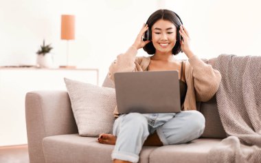 İşten ya da okuldan ayrıl. Gülümseyen Asyalı kadın müzik dinliyor, oturma odasında kanepede dinleniyor. Milenyum kadını en sevdiği şarkıyı seviyor, koltukta oturuyor ve kulaklıklara dokunuyor.