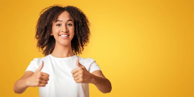 Kullanmayı, iyi bir teklif sunmayı ya da harika bir teklif sunmayı öneriyorum. Beyaz tişörtlü, mutlu, genç, Afro-Amerikan kadın. Sarı arka planda izole edilmiş, stüdyo çekimi.