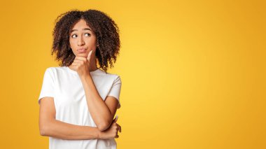 Akıllı öğrenci, iş kadını ya da blog yazarı karar verir. Beyaz tişörtlü düşünceli Afro-Amerikan kadın kıvırcık saçlı, el pençe dize, sarı arka planda izole edilmiş, stüdyo çekimi