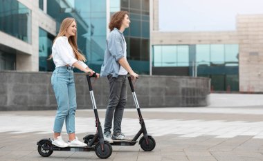 Şehirde elektrikli scooter kullanan, birlikte takılan gülümseyen genç bir çiftin profili. Mutlu adam ve kadın dışarıda geziyor, hafta sonları vakit geçiriyor.