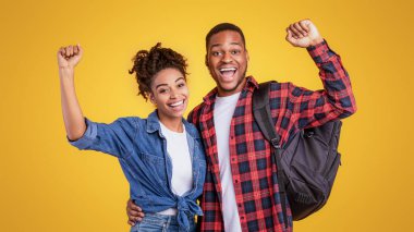 Yolculuğun neşesi. Sırt çantalı mutlu siyah turist çifti, sarı stüdyo arka planında, 