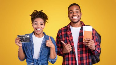 Tatil kavramı. Sarı arka planda duran mutlu siyah çift fotoğraf makinesi ve seyahat biletleri. Stüdyo Çekimi